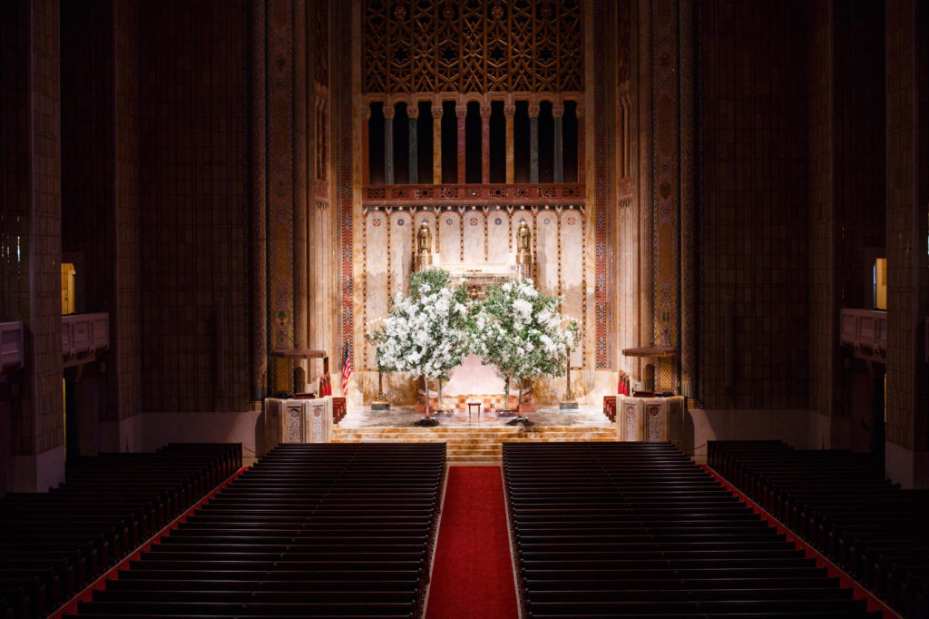 Interior view of an event venue space, a church sanctuary with a red carpet aisle leading to an altar adorned with white flowers.