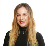 Smiling woman with long blonde hair wearing a black top and a necklace, ready to attend an event at one of the premier event venue spaces.