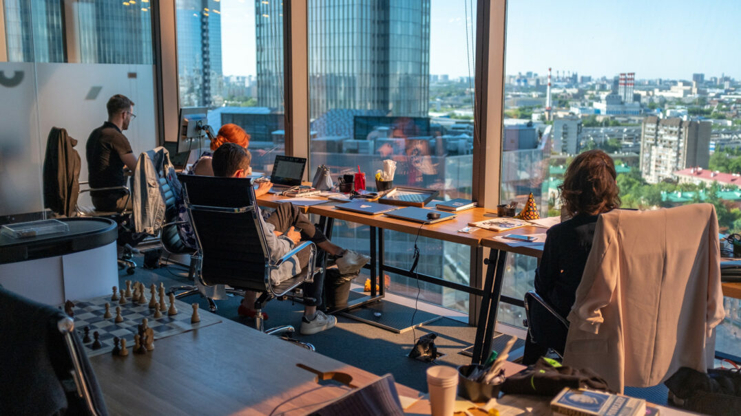 Office workers at desks with computers, overlooking a cityscape through large windows in an event planning company.