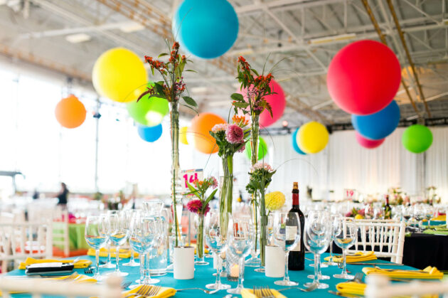 Festively decorated banquet table with colorful balloons and floral centerpieces arranged by an event planning company.