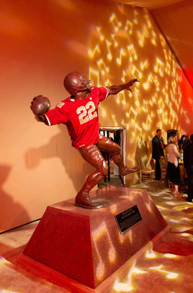 A bronze statue of a football player in a throwing pose displayed against a lit, patterned background in one of the premier event venue spaces.