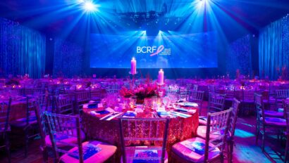 Elegant gala dinner setting with blue lighting and BCRF event branding onstage hosted by a leading event planning company.