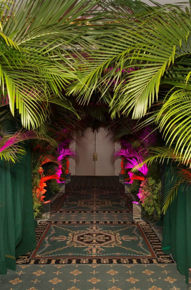 Event planners designed a tropical themed event entrance with illuminated archway of palm leaves and flowers.