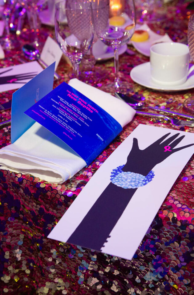 A decorated event table arranged by an event planning company with a sequined tablecloth, place settings, and event programs.