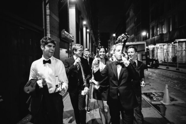 group of people dressed in formal wear laughing and walking down the street.