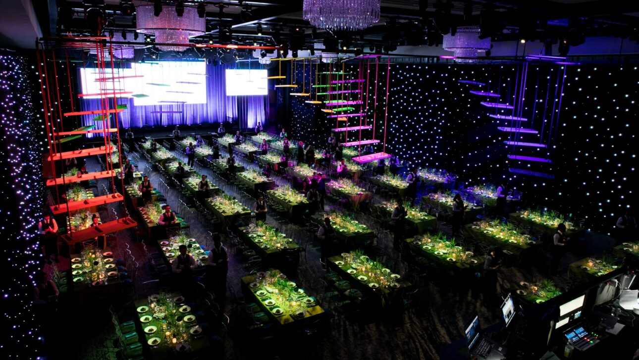 Elegant event venue space set up for a formal dinner with colorful lighting and a stage with large screens.