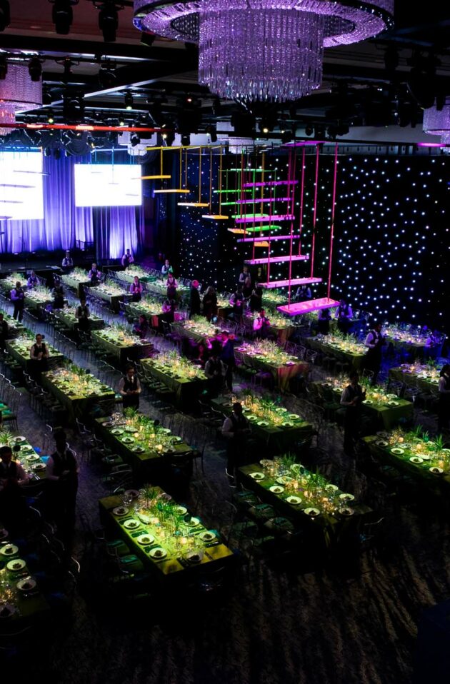 Elegant event venue space set up for a formal dinner with colorful lighting and a stage with large screens.