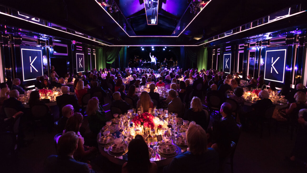 An elegant gala organized by a top event planning company with guests seated at round tables in a venue illuminated with purple and blue lights.