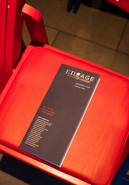 An event program designed by a leading event planning company, titled "ensage", rests on a red chair.