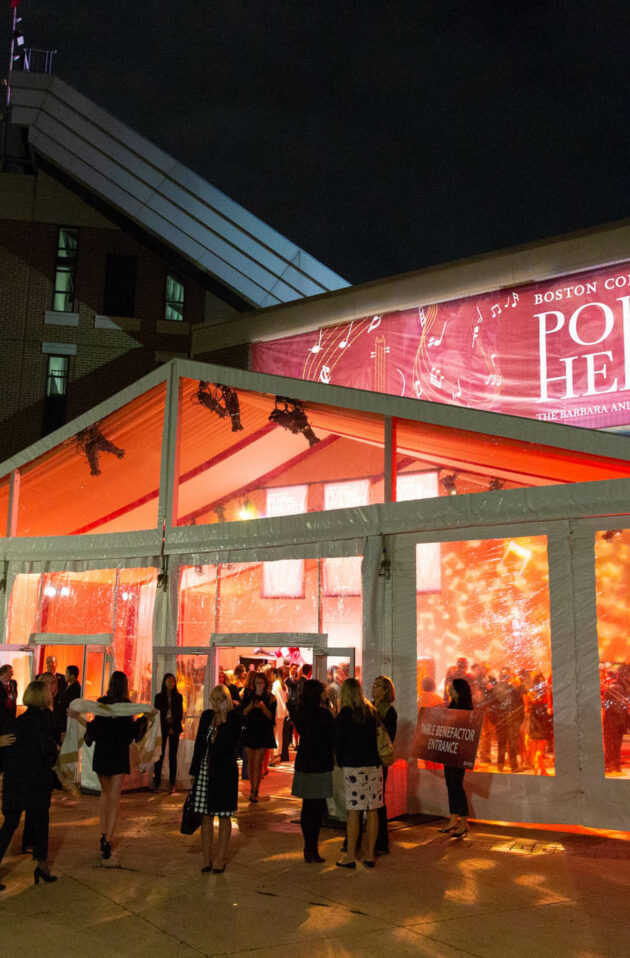 Guests gather outside a lit tent for the "pops on the heights" event at Boston College, meticulously organized by a premier event planning company.