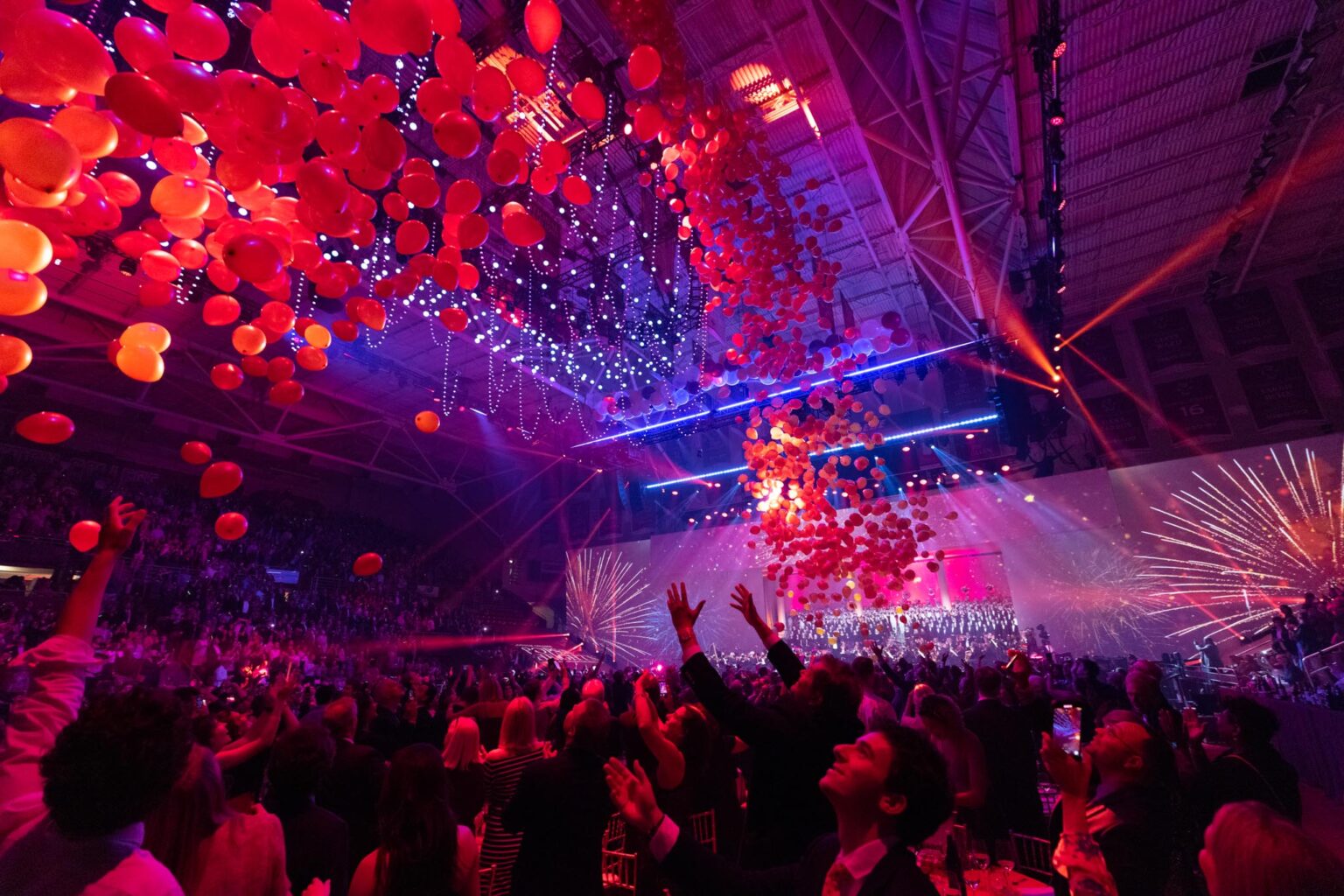 Audience enjoying a vibrant event organized by the event planning company, with fireworks and a ceiling adorned with red balloons.