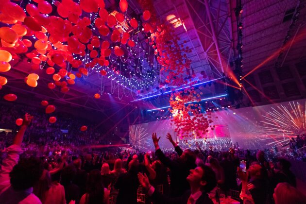 Audience enjoying a vibrant event organized by the event planning company, with fireworks and a ceiling adorned with red balloons.