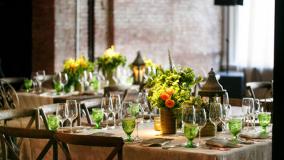 An elegantly set dining table with green glassware and vibrant floral centerpieces in a room with brick walls, meticulously arranged by expert event planners.