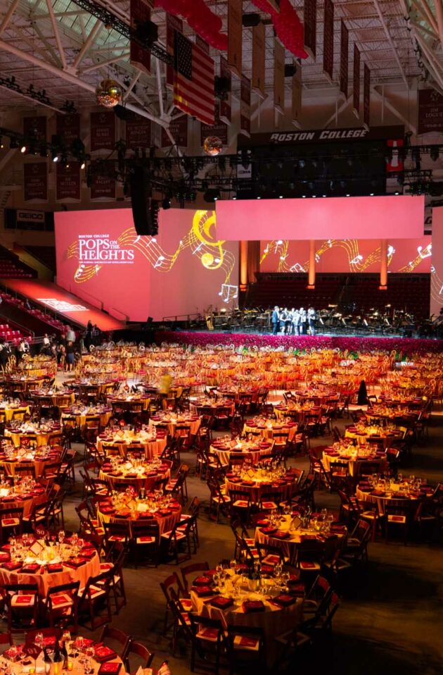 A gala event organized by professional event planners, set up with dining tables in an indoor arena, featuring a stage for performances.