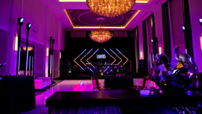 An event venue space lit with purple ambient lighting featuring a stage with geometric patterns and chandeliers.