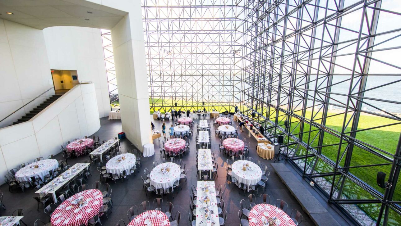 glass-walled building with tables set for a party inside.