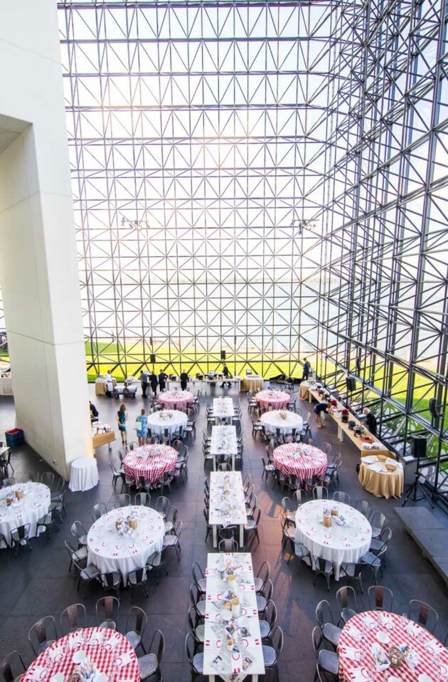 glass-walled building with tables set for a party inside.