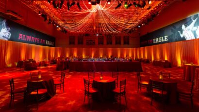 A banquet hall prepared by an event planning company for an event with tables, chairs, and dramatic red lighting with a banner that reads "always an eagle.