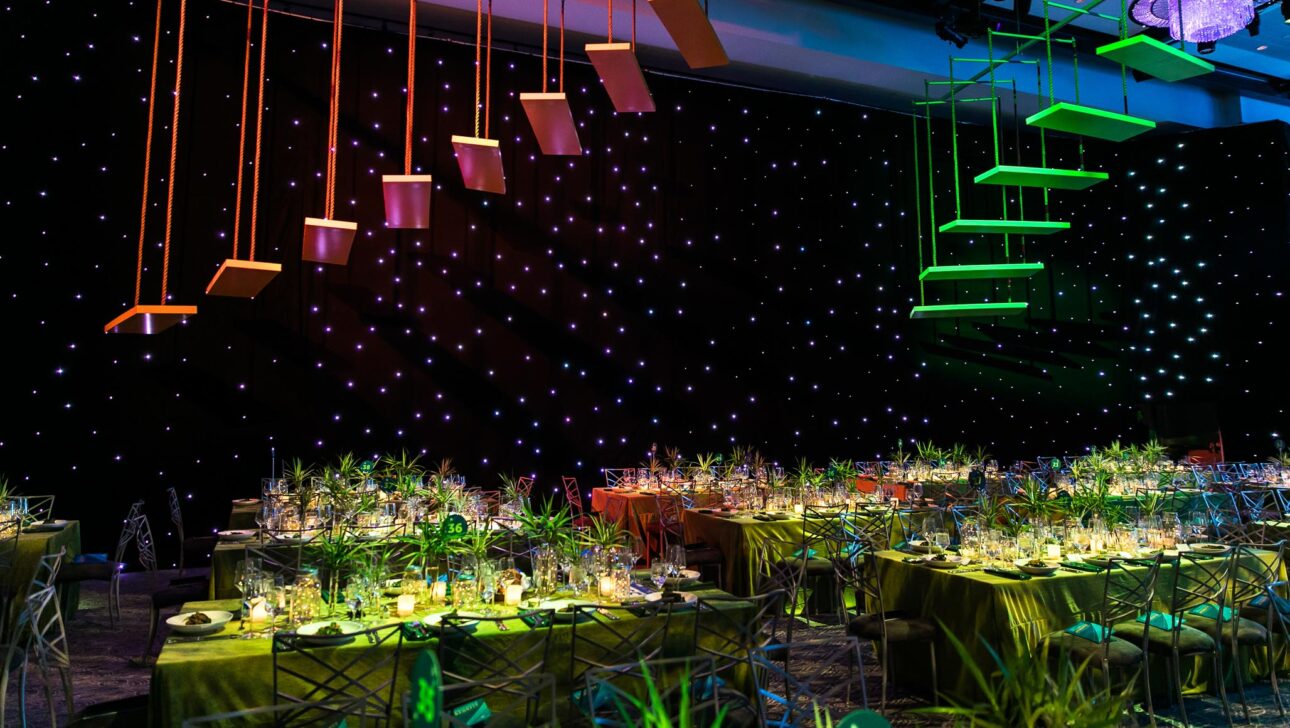 neon colored stairs hanging in the air over decorated tables in a dark room.