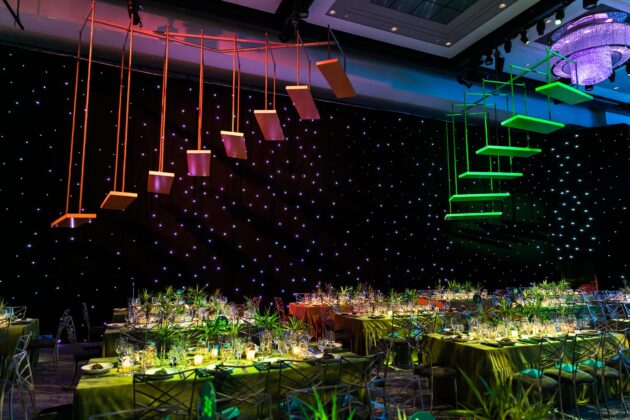 Elegant event venue space decorated with hanging geometric shapes and a starry backdrop with tables set for a formal occasion.