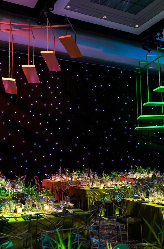 neon colored stairs hanging in the air over decorated tables in a dark room.