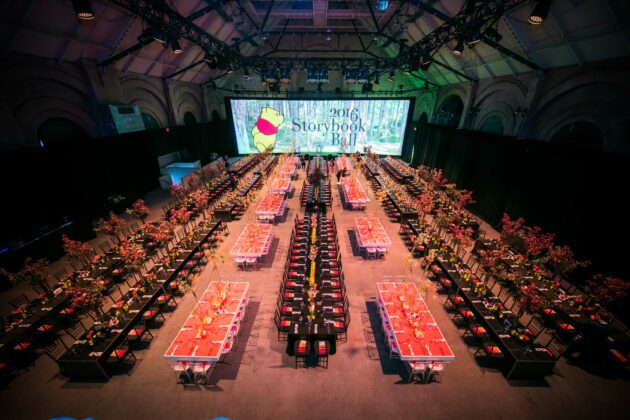 large hall full of decorated dining tables with a screen at the back that says storybook ball 2016.