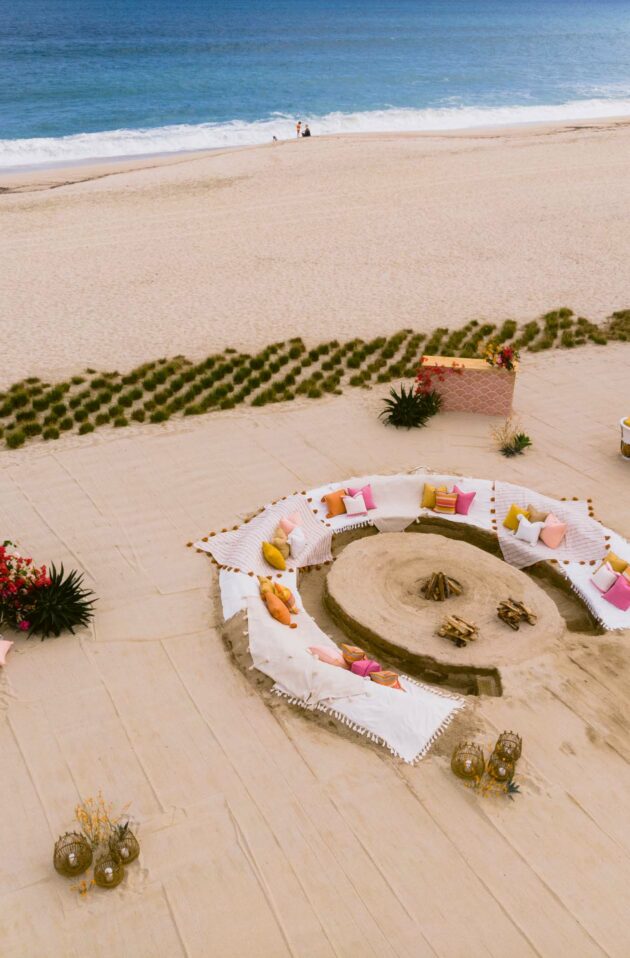 Aerial view of a beach wedding setup organized by an event planning company, with circular seating arrangement and a floral arch.