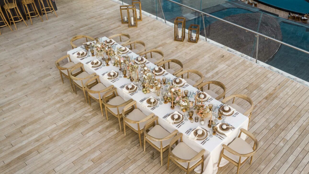 An elegantly set outdoor dining table prepared by a top event planning company, with decorative centerpieces and place settings, overlooking a pool area.