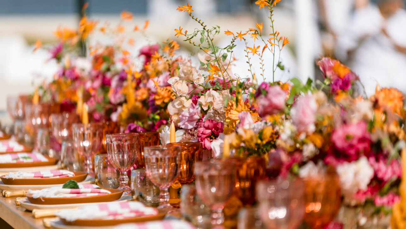 Elegantly set table in an event venue space with vibrant floral centerpieces and matching glassware.