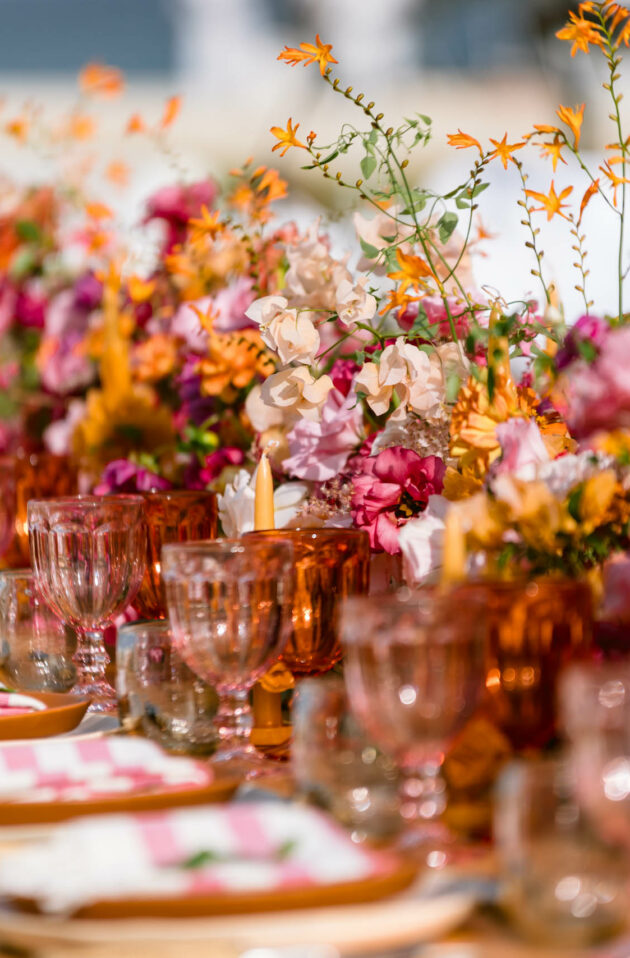 Elegantly set table in an event venue space with vibrant floral centerpieces and matching glassware.