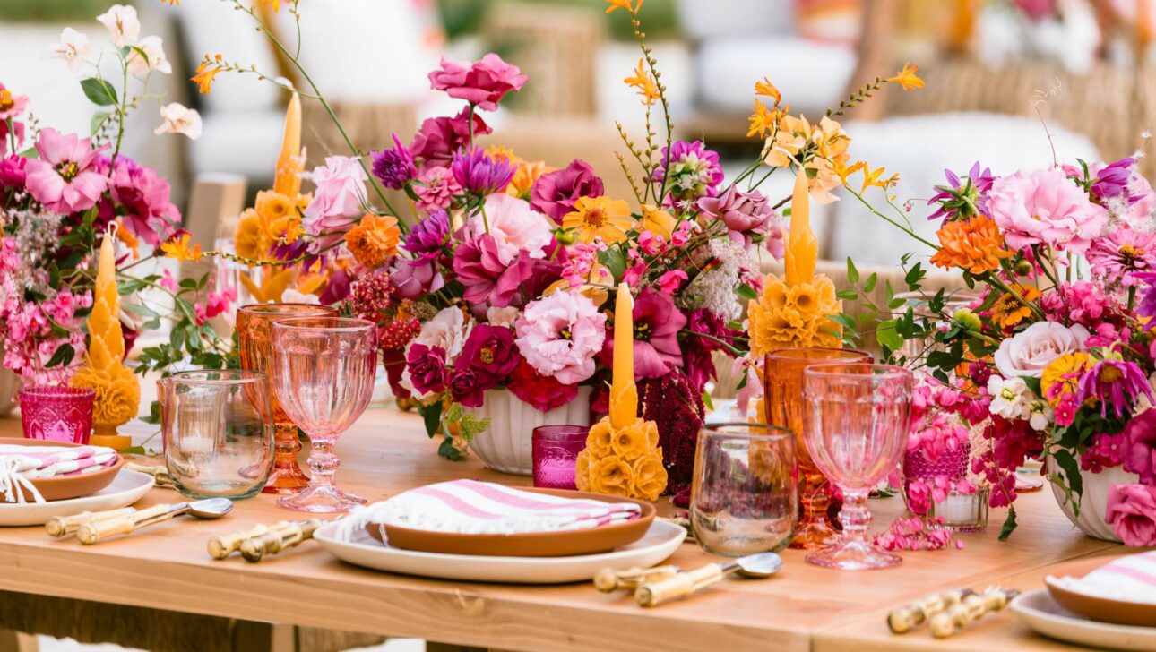 A vibrant outdoor table setting with colorful floral arrangements and pink glassware, perfectly curated by a leading event planning company.