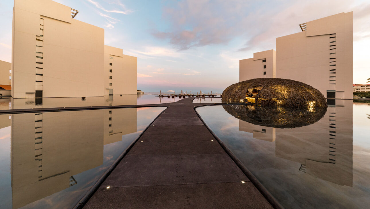 Modern architectural complex, an event venue space with a spherical art installation reflecting on water at twilight.