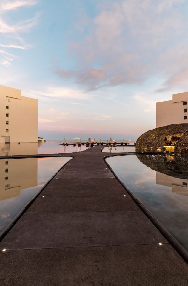 Modern architectural complex, an event venue space with a spherical art installation reflecting on water at twilight.