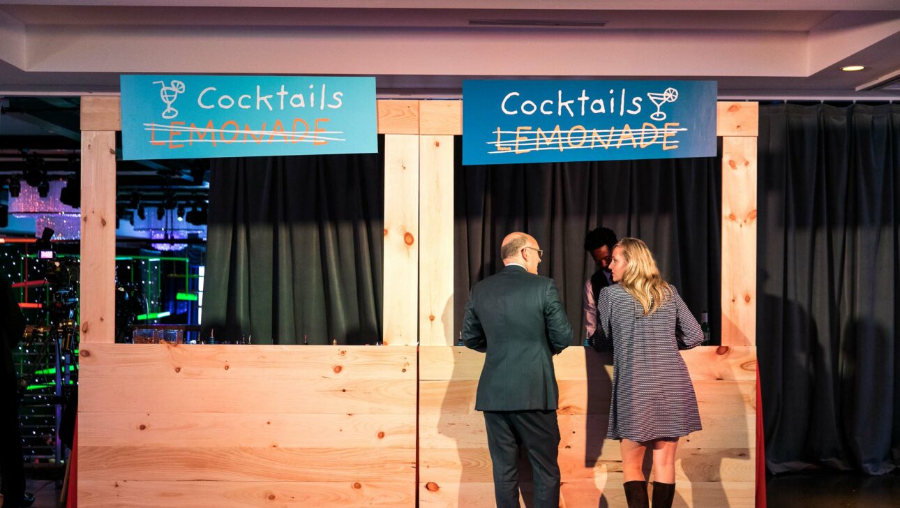cocktail bar decorated like a wooden lemonade stand with a man and woman at it.