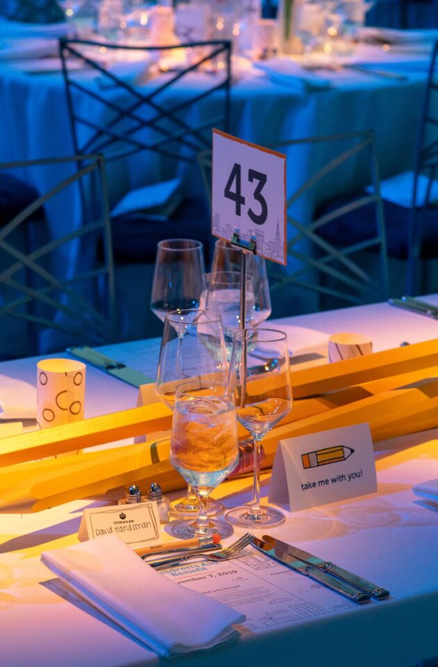 Elegant banquet table set for an event by a professional event planning company, with a numbered centerpiece and soft blue lighting.