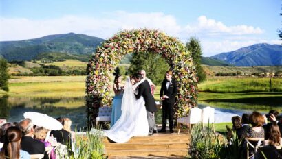 bride and groom kissing in their wedding under a floral arch outside.