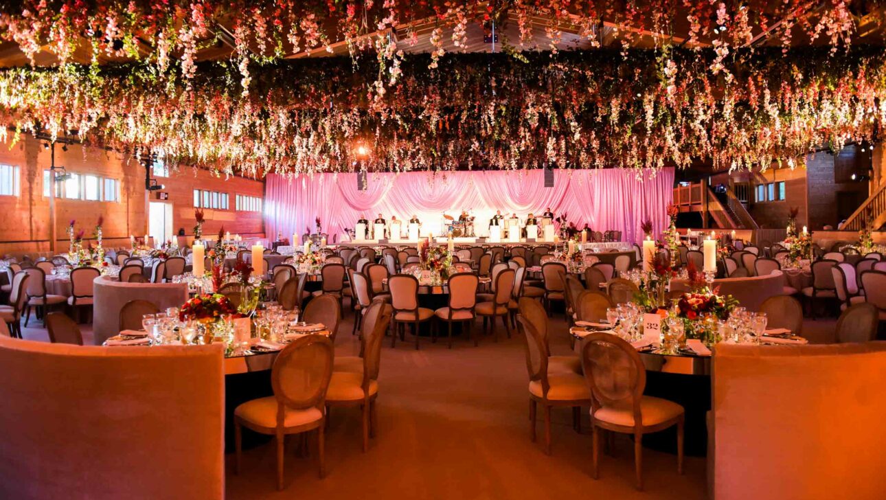 Elegant banquet hall adorned with floral arrangements and a pink draped backdrop, set up by an event planning company for a formal event.