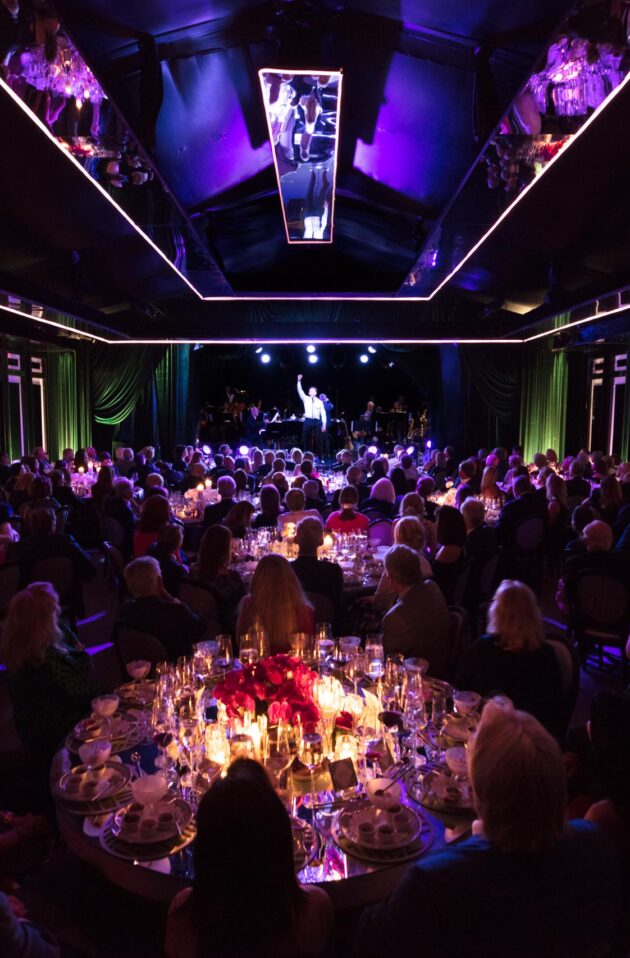 Guests seated at a formal gala dinner organized by an event planning company, with a stage in the background.