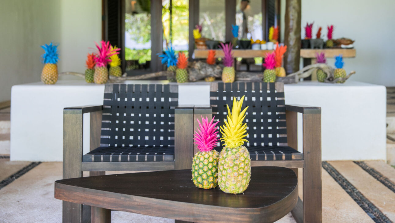 two pineapples on a coffee table in front of two lounge chairs.