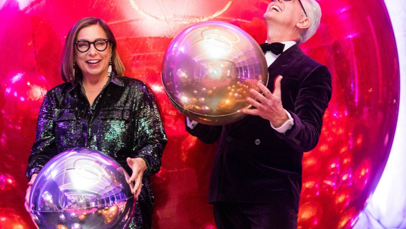 Two event planners at a festive gathering with metallic balloons, one playfully balancing a balloon on their finger.