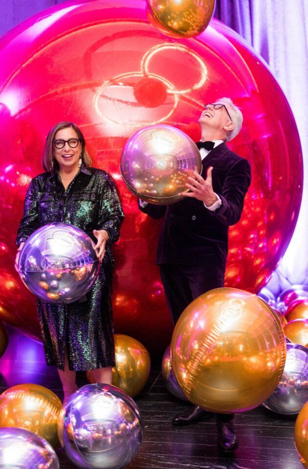 Two event planners at a festive gathering with metallic balloons, one playfully balancing a balloon on their finger.