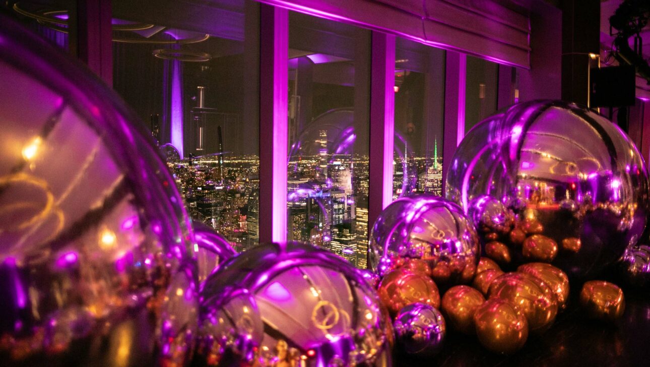 large reflective balls on the floor in a dark neon lit room looking out windows over a city skyline.