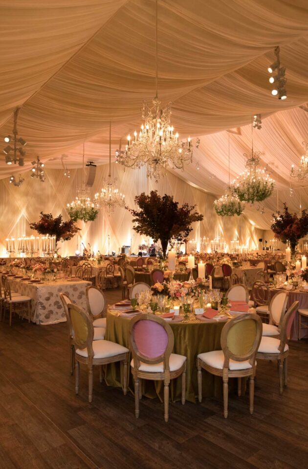 An elegantly decorated event venue space with chandeliers, draped ceiling, and tables set for an event.