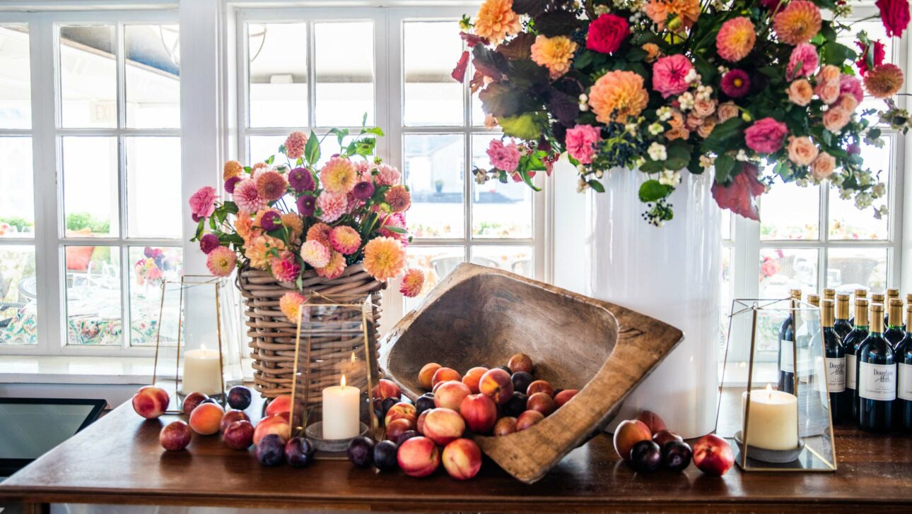 Elegant dining setting with vibrant floral arrangements, fresh fruit, candles, and wine bottles, creating a festive atmosphere curated by an event planning company.