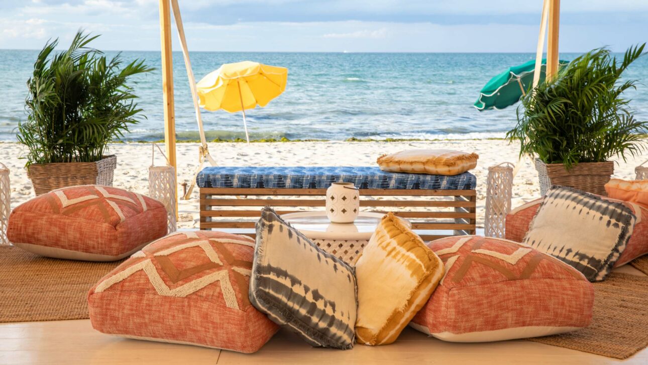 Cozy beachfront event venue space with cushions, plants, and colorful umbrellas with a view of the sea.