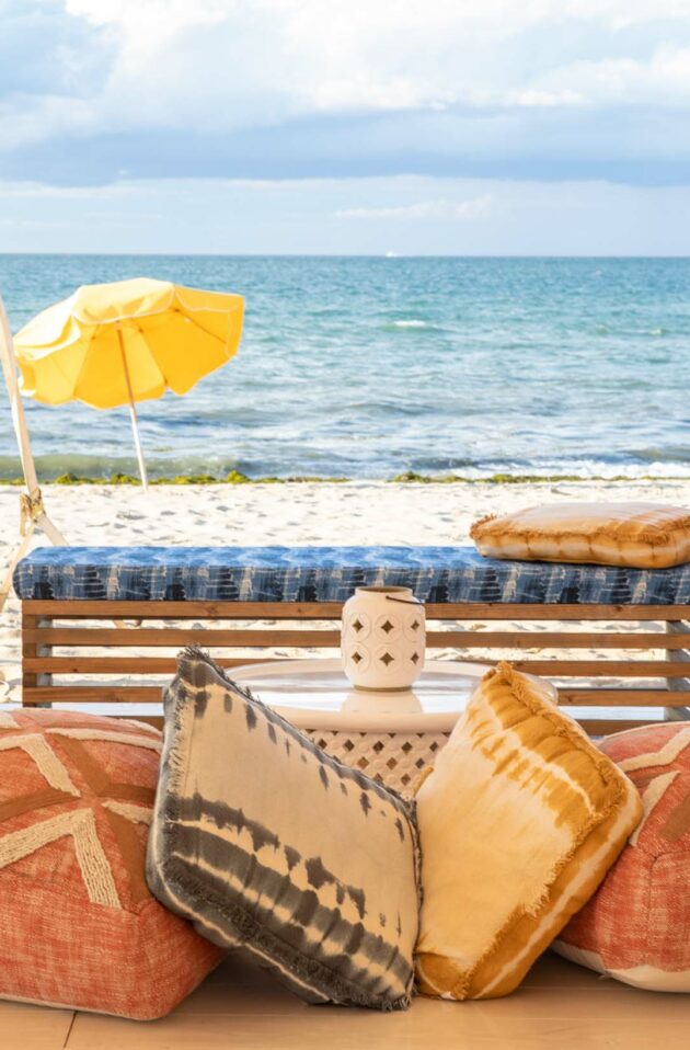 Cozy beachfront event venue space with cushions, plants, and colorful umbrellas with a view of the sea.