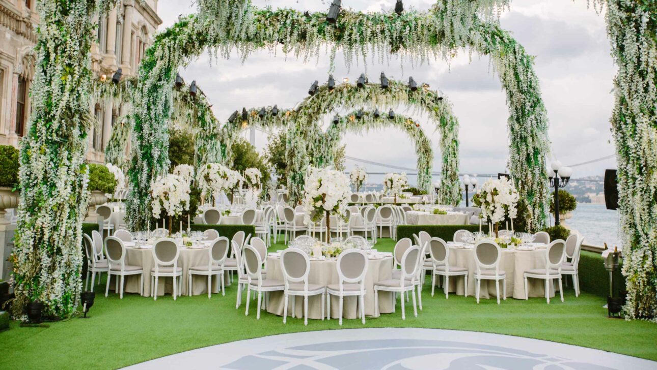 decorated round tables under floral arches next to the water.