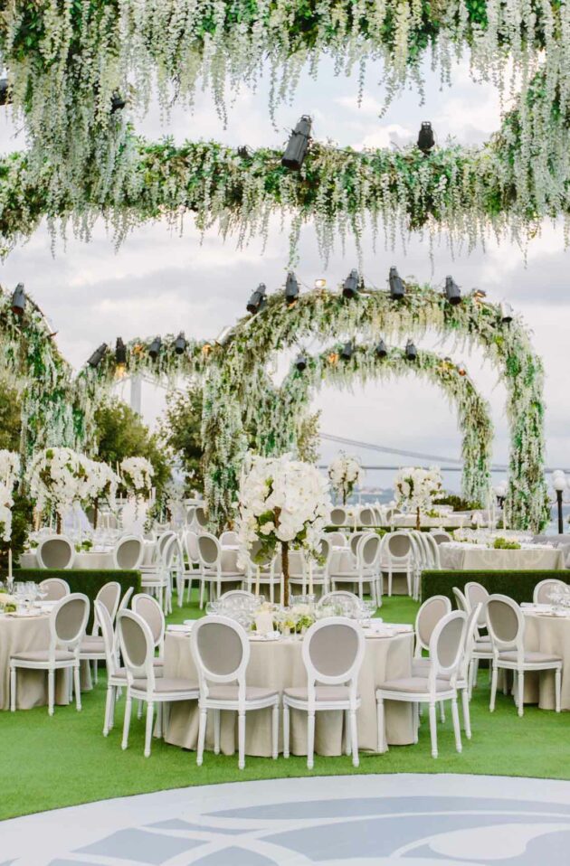 decorated round tables under floral arches next to the water.