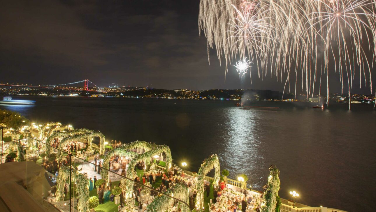 fireworks over a river with a party in the foreground under floral arches.
