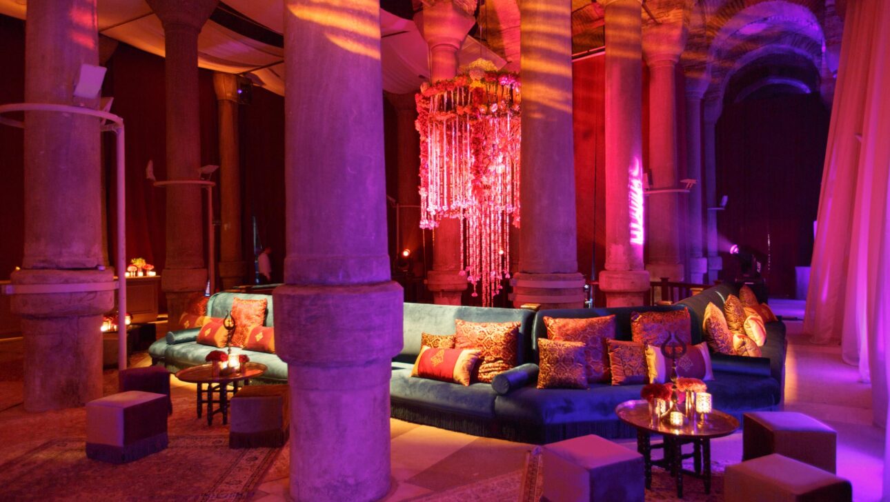 Lavishly decorated lounge with a plush sofa and mood lighting inside an event venue space with classical columns.